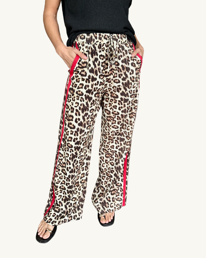 Person wearing leopard print pants with red trim in a home setting